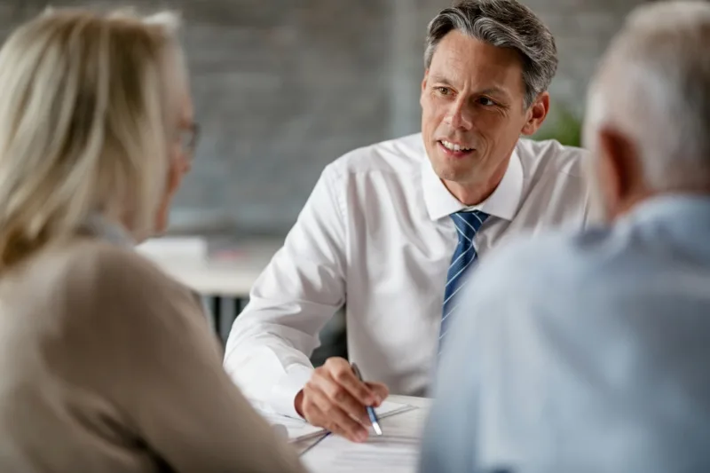 Homme chemise cravate en train de discuter avec un couple que l'on aperçoit de dos - Photo d'illustration située sur page d'accueil d'Article 66-5 qui est un service de création de site web pour avocat