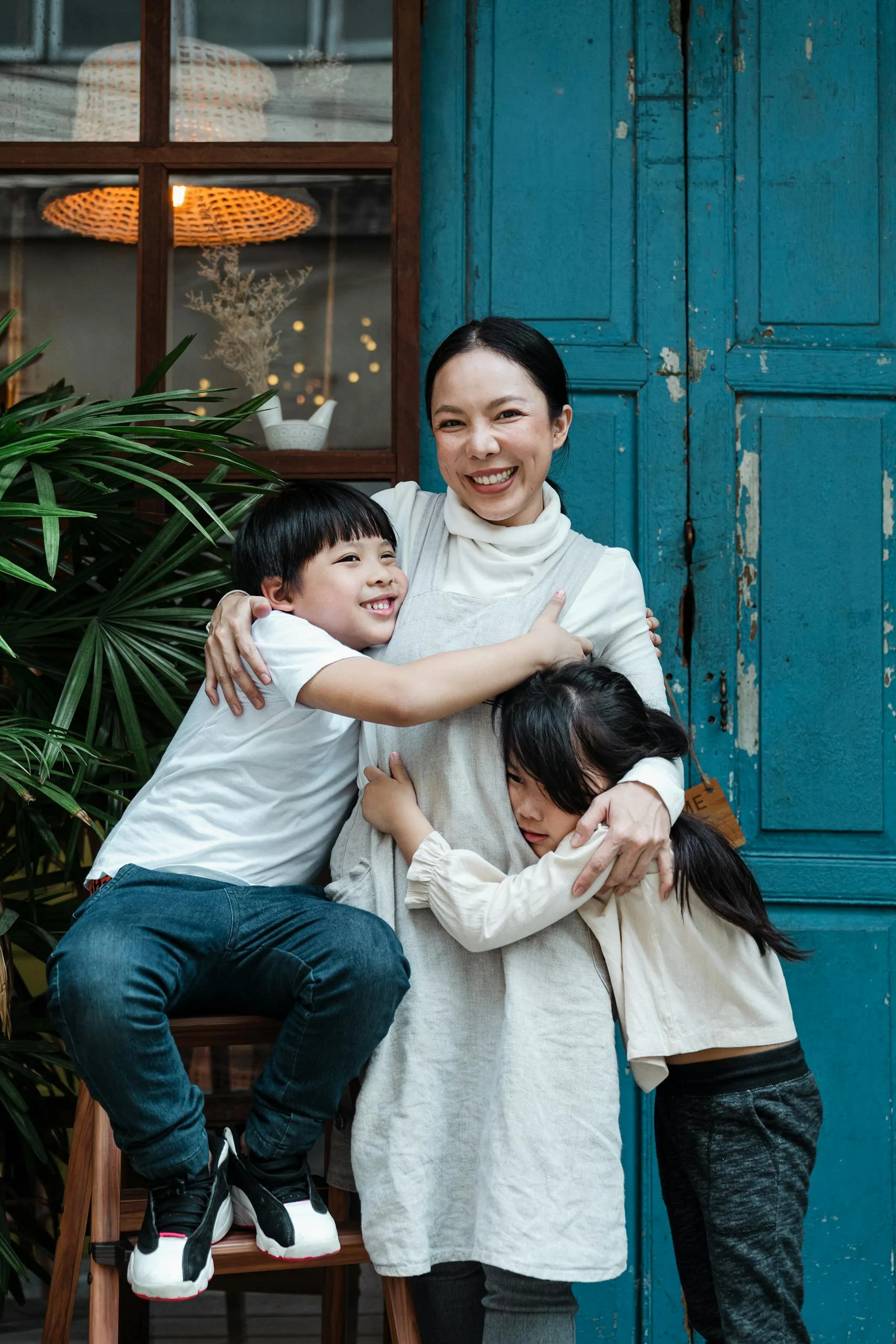 A joyful mother hugging her two children against a rustic blue door outdoors.