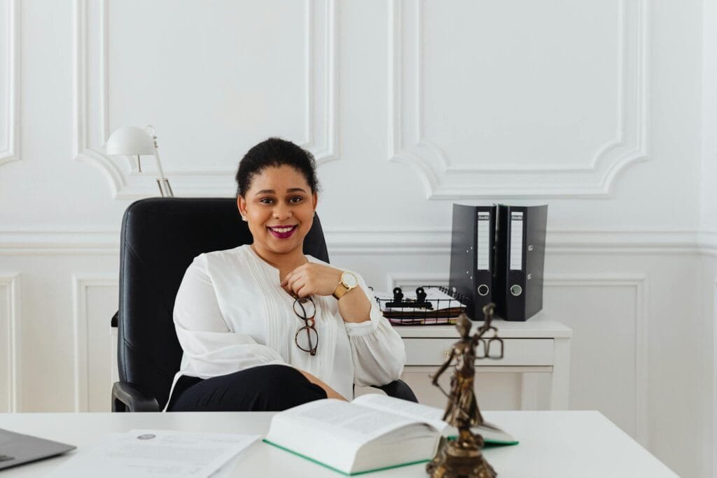 Confident woman in a professional office setting with legal books and statue, exuding a sense of authority.