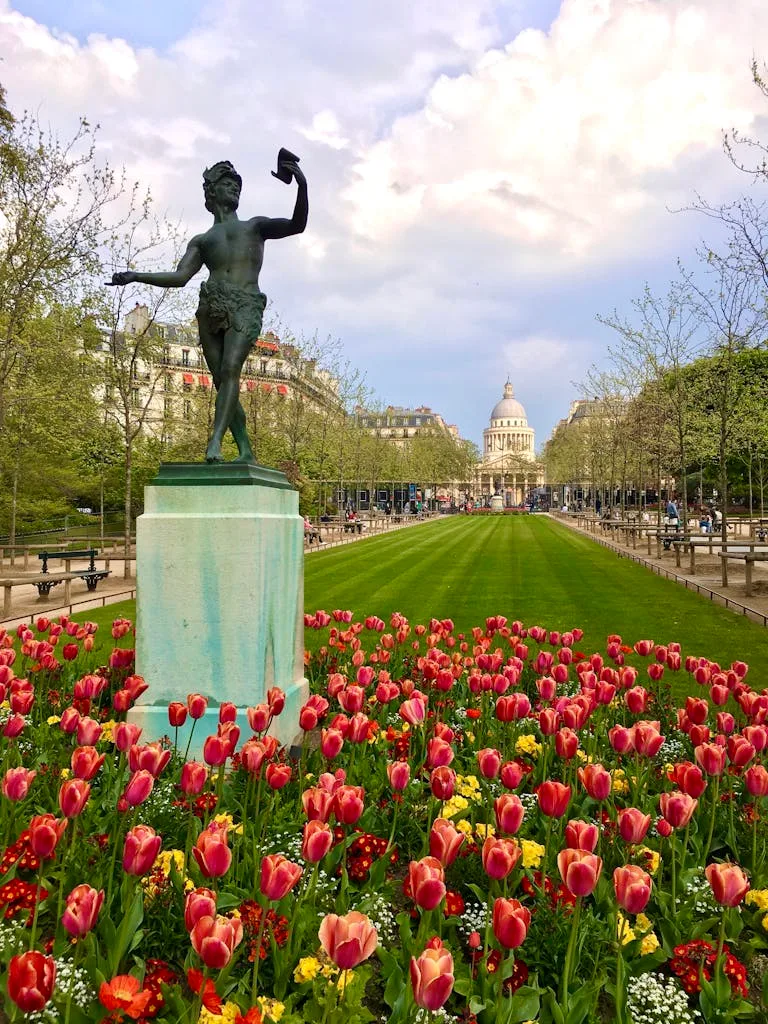 Beautiful view of Luxembourg Gardens with a statue and blooming tulips under a cloudy sky in Paris.