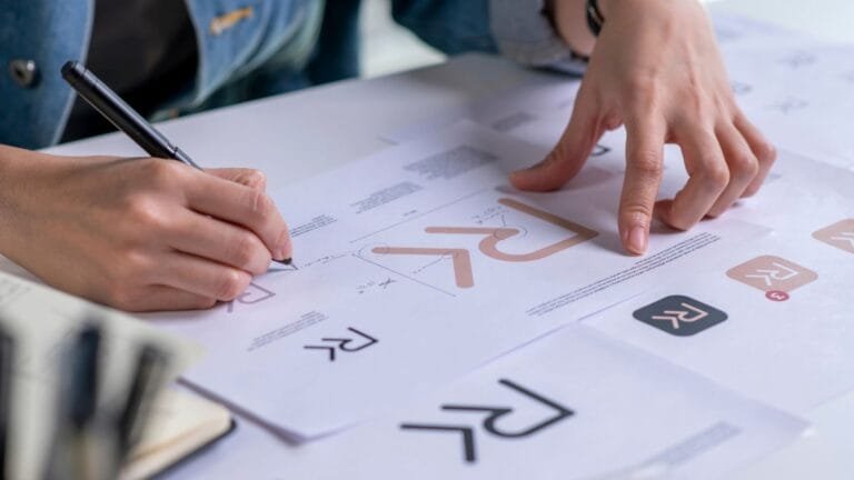 Designer travaillant sur la déclinaison de logos pour l’identité visuelle d’un cabinet d’avocat, plan serré sur les mains corrigeant des maquettes imprimées.